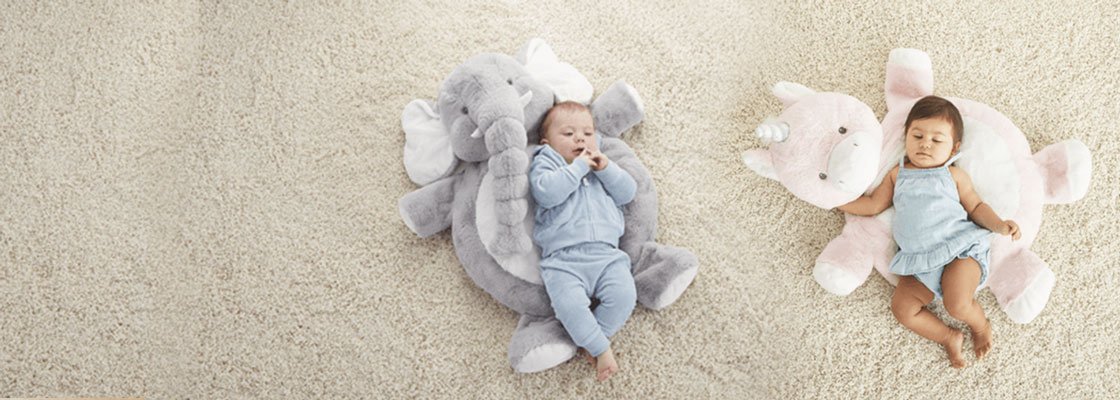 boy baby and girl baby lying on stuffed animal mats on a cream carpet